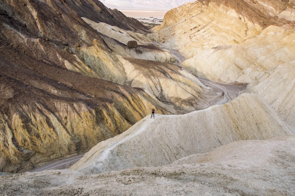 "A lone hiker standing on a ridge in a rugged desert canyon with layered, eroded rock formations."